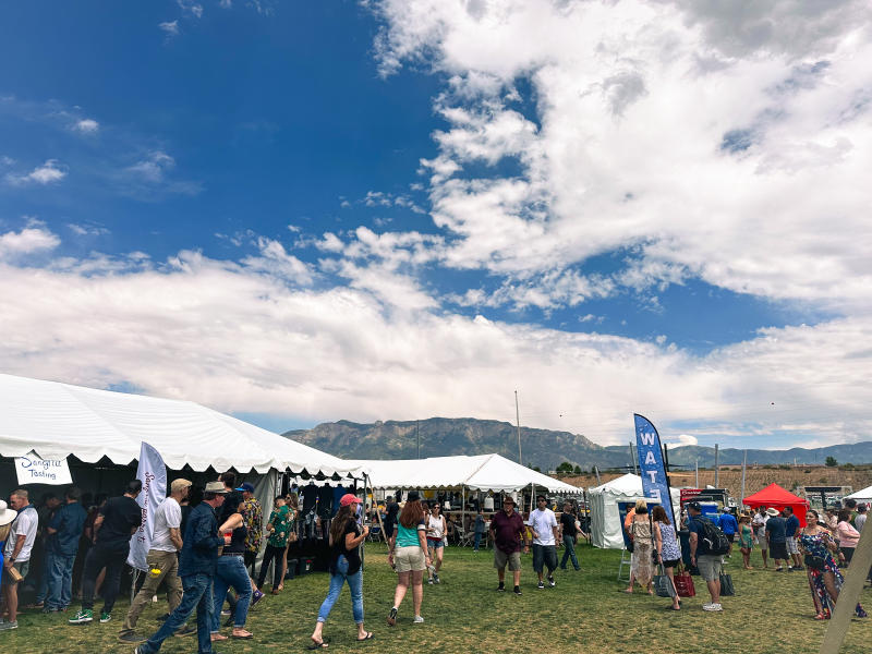 View of the Albuquerque Wine Festival. There are many people walking between white tents offering wine tastings.